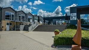 A modern building with a restaurant sign, outdoor seating, and a staircase leading to the entrance. - Skærbækcentret (Skaerbaek)