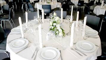 A round table set for a formal event with white tablecloths, plates, cutlery, and candles.