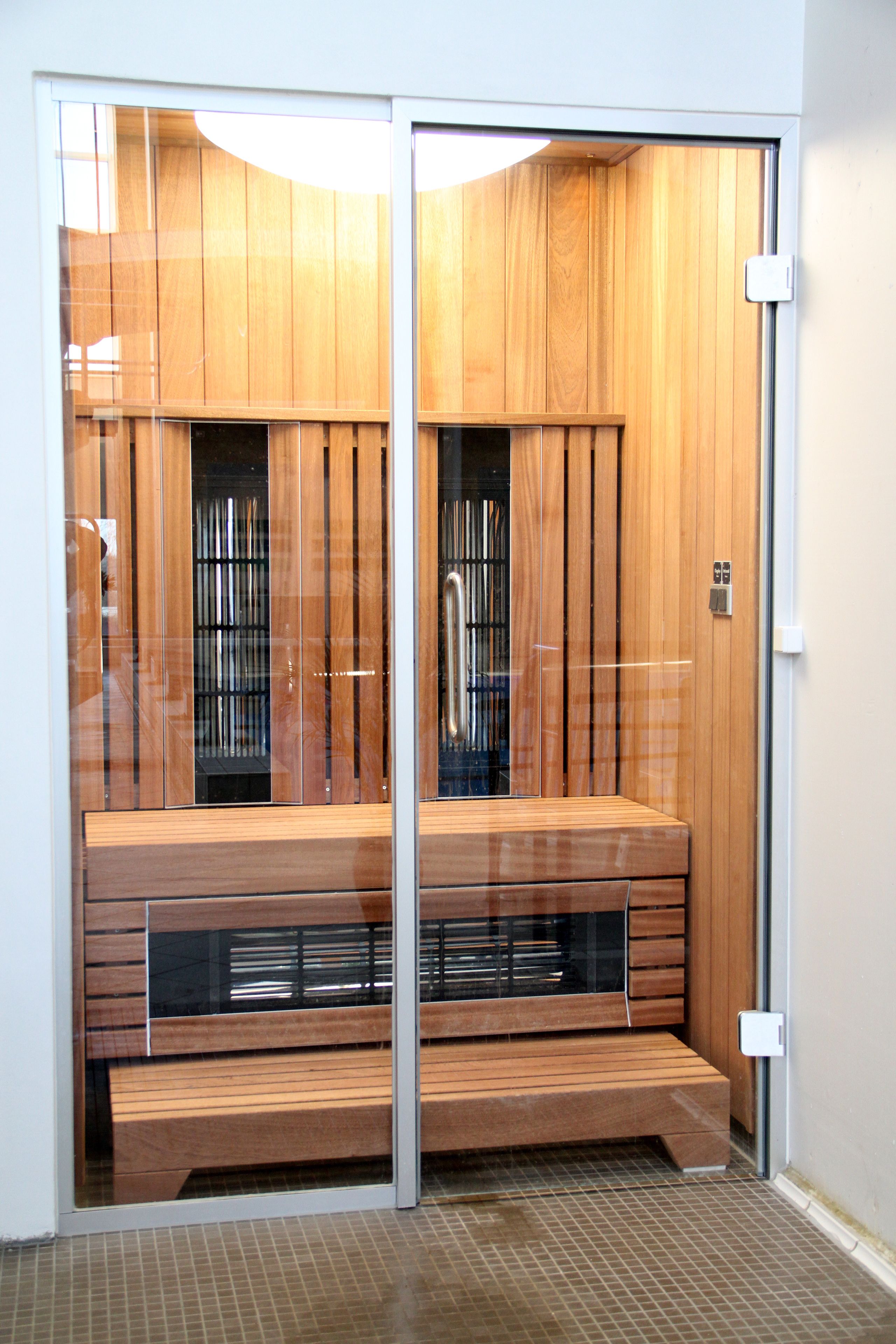 Una sauna con paneles de madera, un banco y una puerta de vidrio.