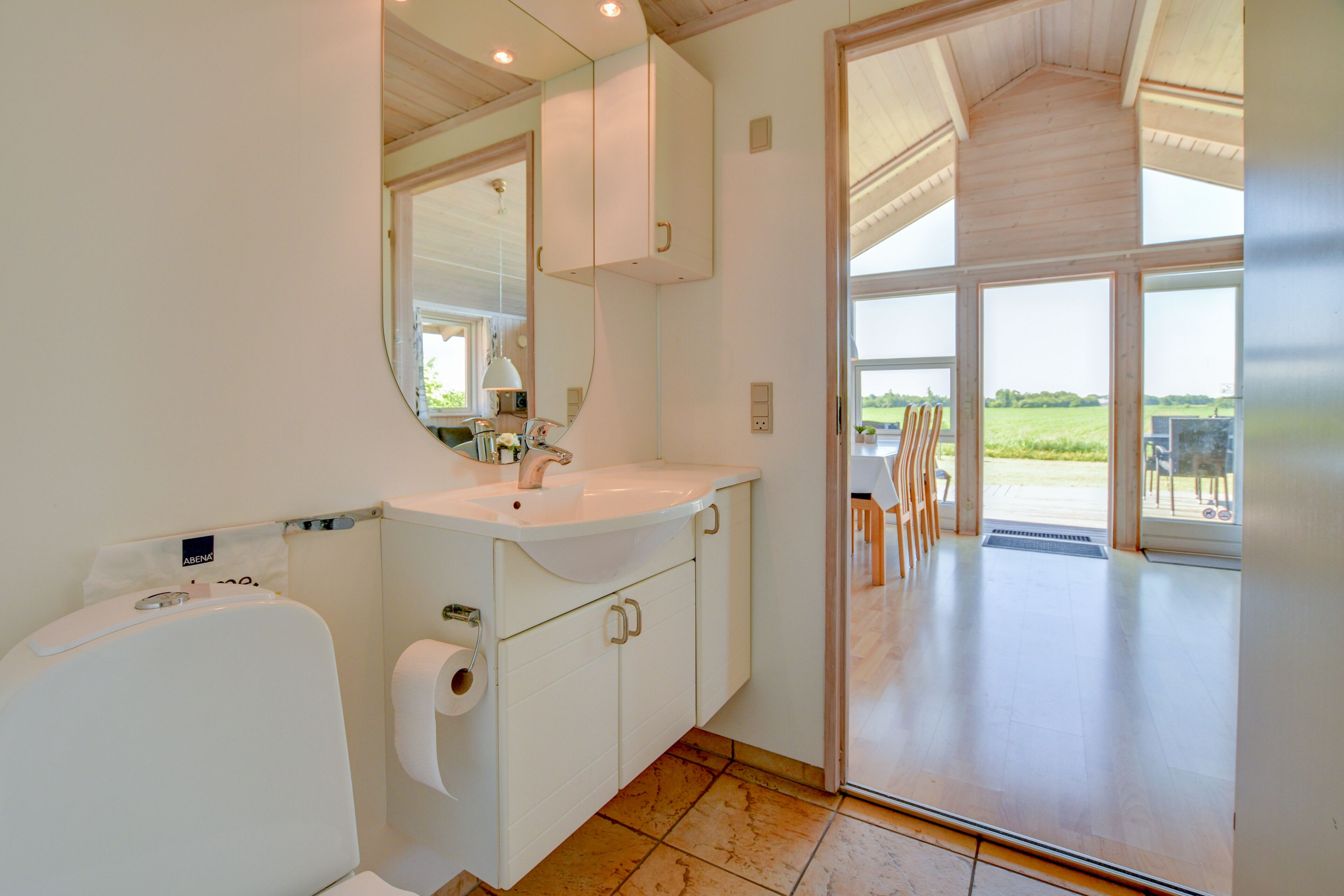Un bagno moderno con un grande specchio, un lavandino bianco e mobili contenitori. Si apre su un patio con mobili da esterno.