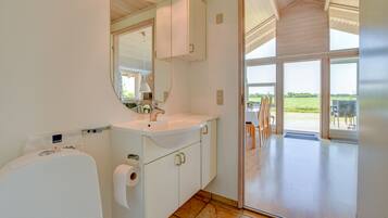 Un bagno moderno con un grande specchio, un lavandino bianco e mobili contenitori. Si apre su un patio con mobili da esterno.