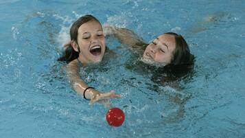 Two people in a swimming pool playing with a red ball.