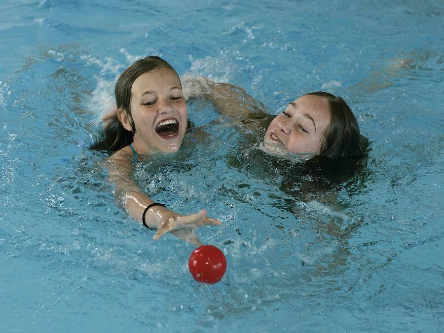 Two people in a swimming pool playing with a red ball.