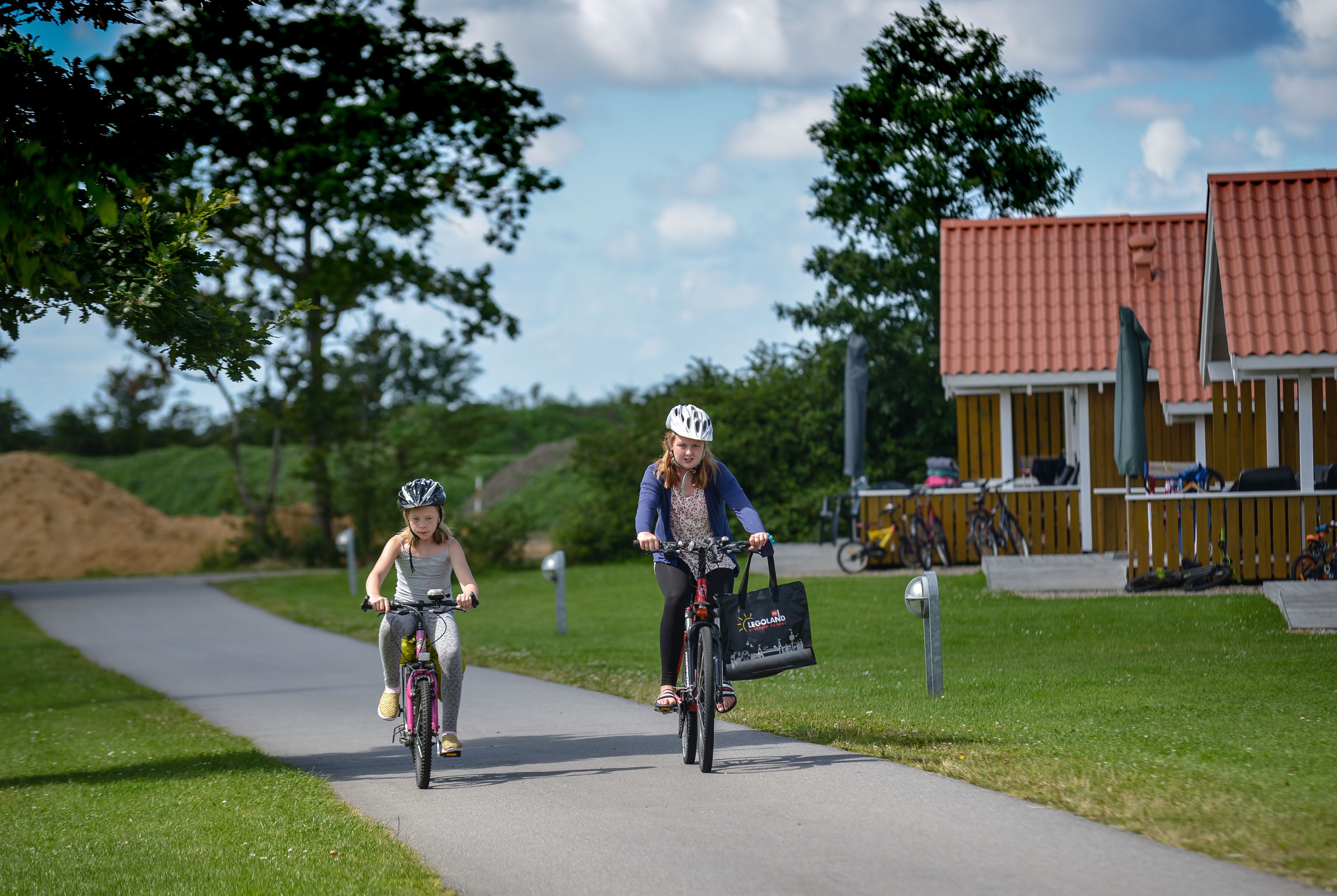 Two people riding bicycles on a paved path with grass on either side.