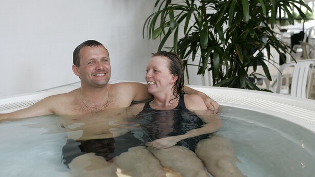 A couple in a hot tub with a plant in the background. - Skærbækcentret (Skaerbaek)