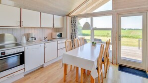 A modern kitchen with white cabinets, a Bosch oven, and a dining area with a white table and wooden chairs. - Skærbækcentret (Skaerbaek)