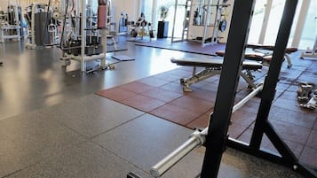 A gym with various exercise equipment, including weight machines and free weights, and a large mirror on the wall.
