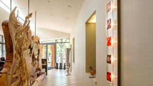 Un hall d’hôtel moderne avec une grande sculpture abstraite, un mur de verre doté de panneaux lumineux et un sol carrelé.