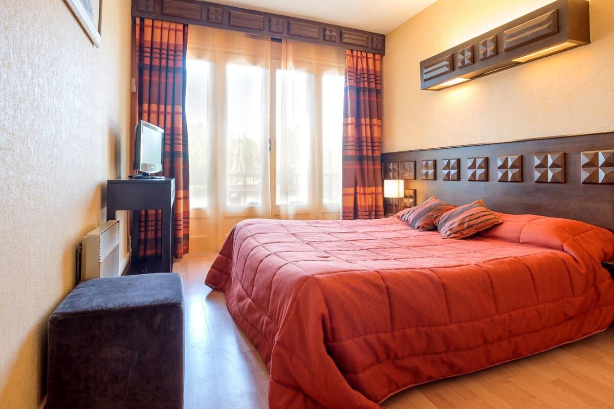 A bedroom with a bed, a desk, a chair, and a window with curtains.