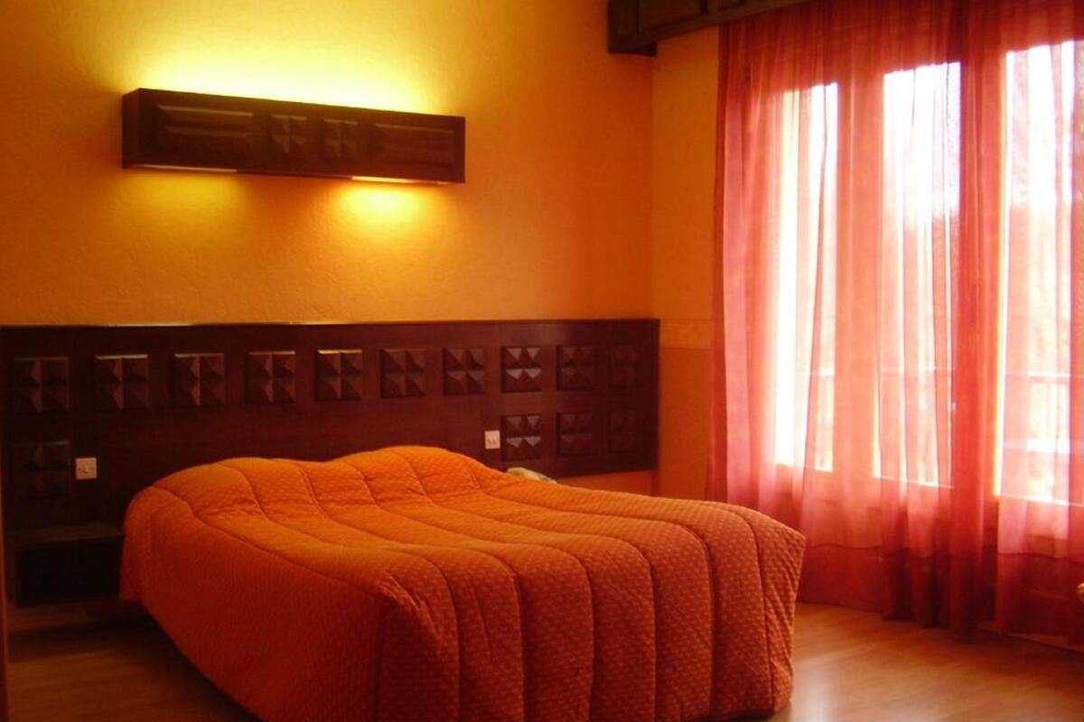 A room with a bed, a wall-mounted light, and a window with curtains.