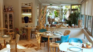 Un restaurant doté de nombreuses tables et chaises, d’un bar avec des bouteilles exposées, et offrant une vue sur la verdure environnante.