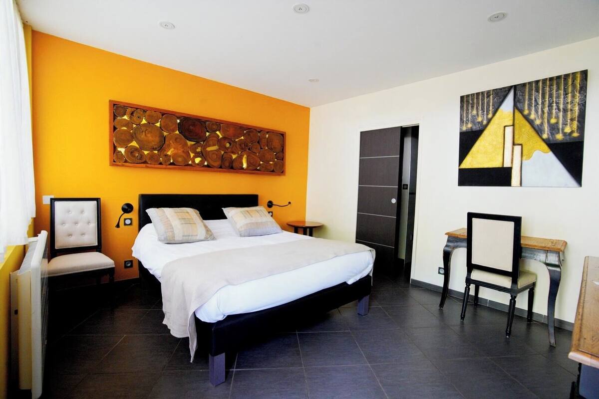A bedroom with a bed, a desk, a chair, a nightstand, and a wall art piece.