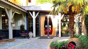 L’entrée d’un hôtel, avec un patio abrité, un palmier et un parterre de fleurs.