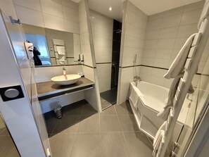 A modern bathroom with a large mirror, a sink, a bathtub, and a shower. - Hôtel Restaurant Chez Nous (Sainte-Croix)