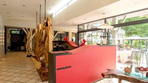 Un comptoir d’accueil avec un panneau rouge, un décor en bois et une vue sur un espace de restauration en plein air.