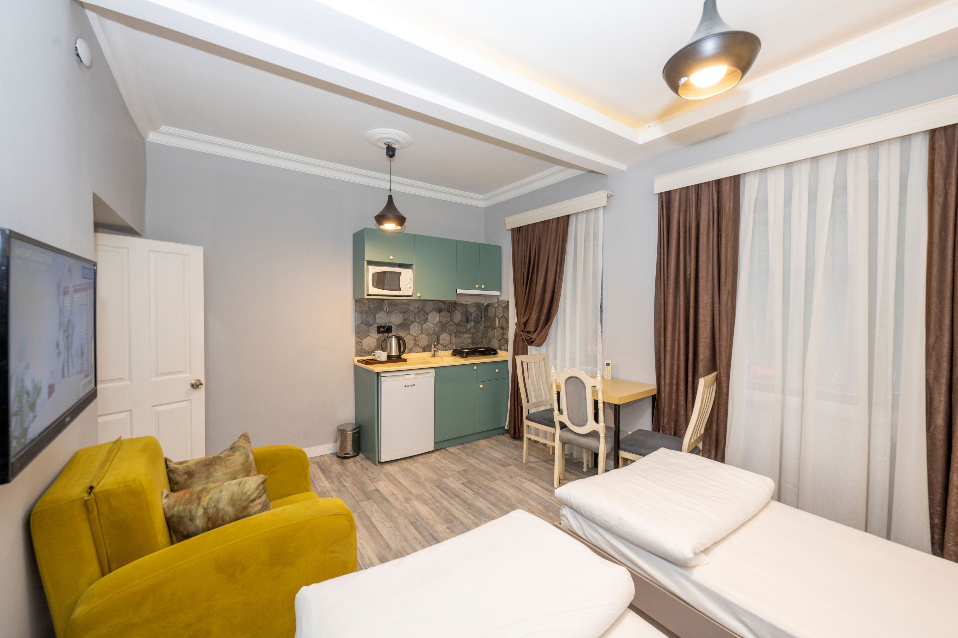 A compact hotel room with a kitchenette, a sofa, a bed, and a dining area.