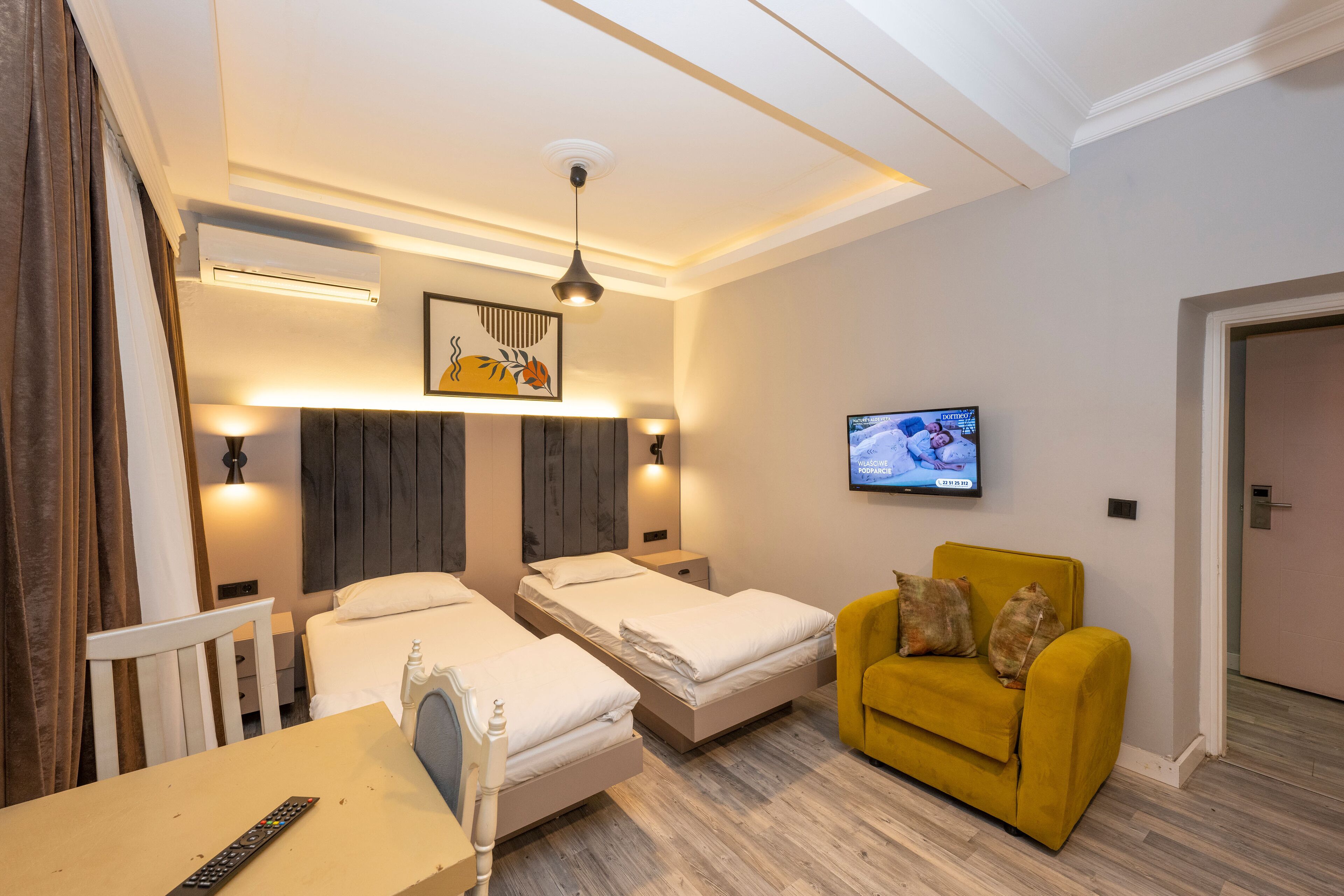 A hotel room with two beds, a yellow armchair, a TV, and a painting on the wall.