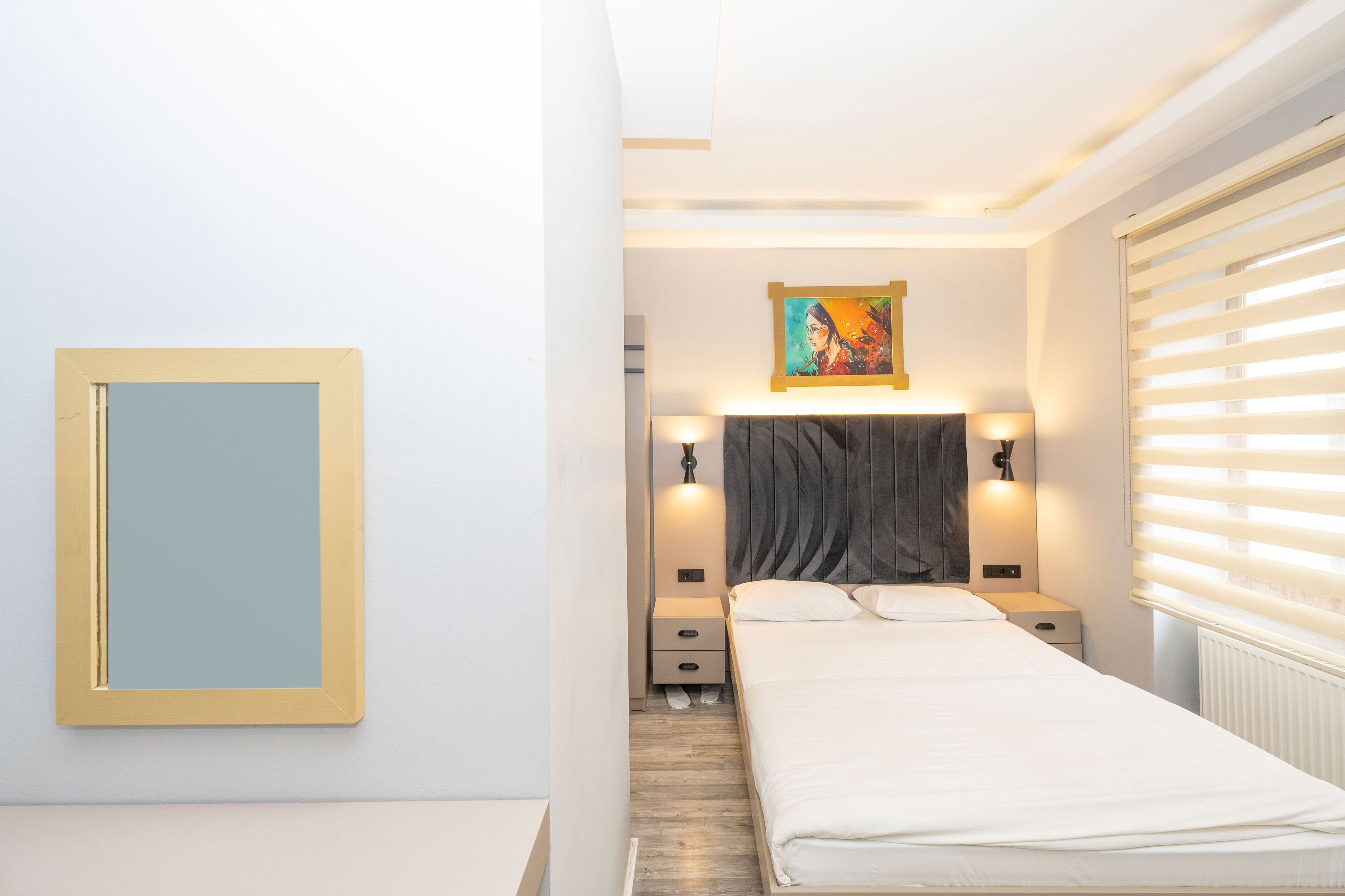 A bedroom with a bed, bedside tables, a nightstand, a mirror, and a painting on the wall.