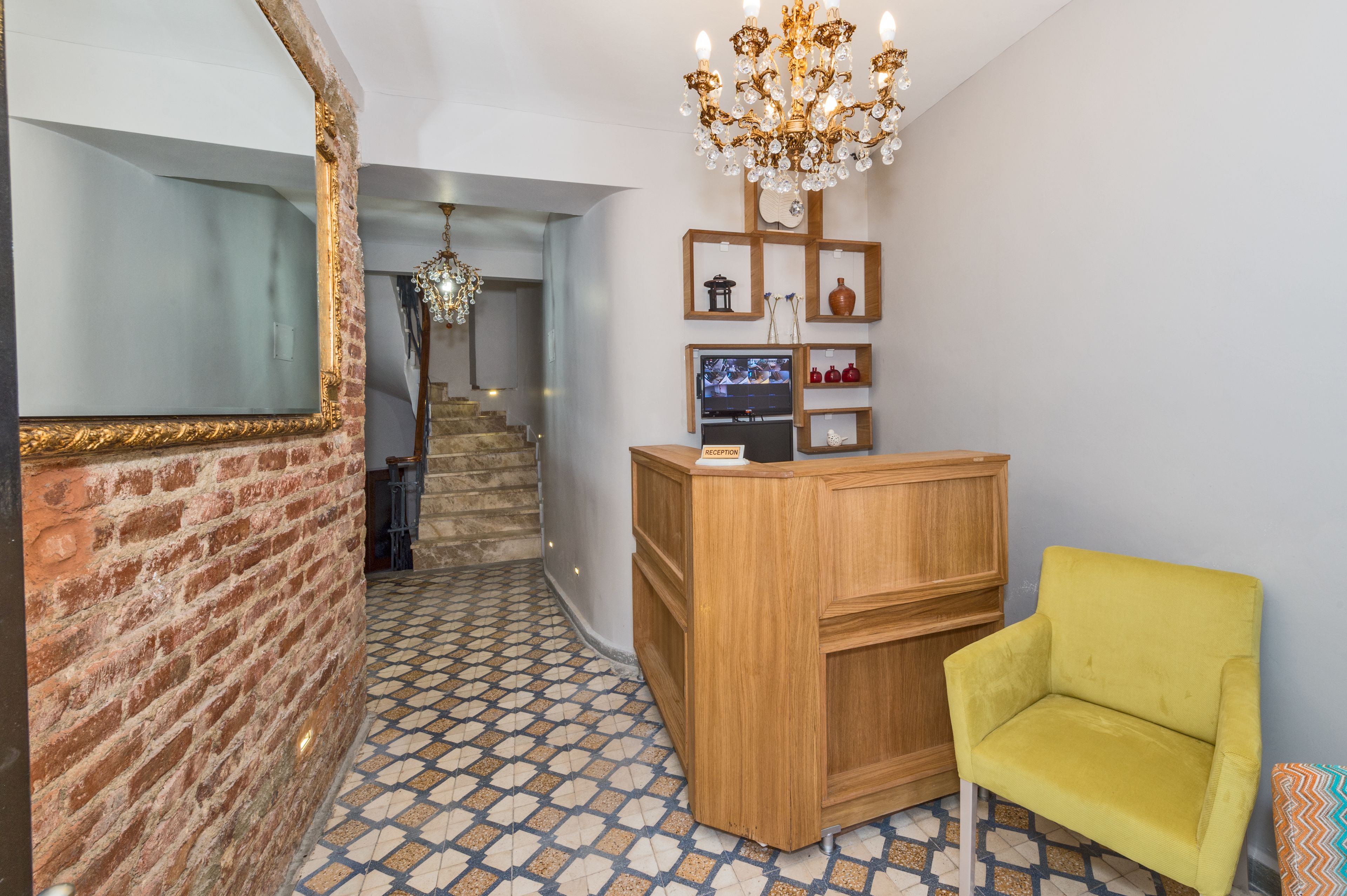Un espace d’accueil avec un bureau en bois, une chaise jaune, un lustre et un escalier en arrière-plan.