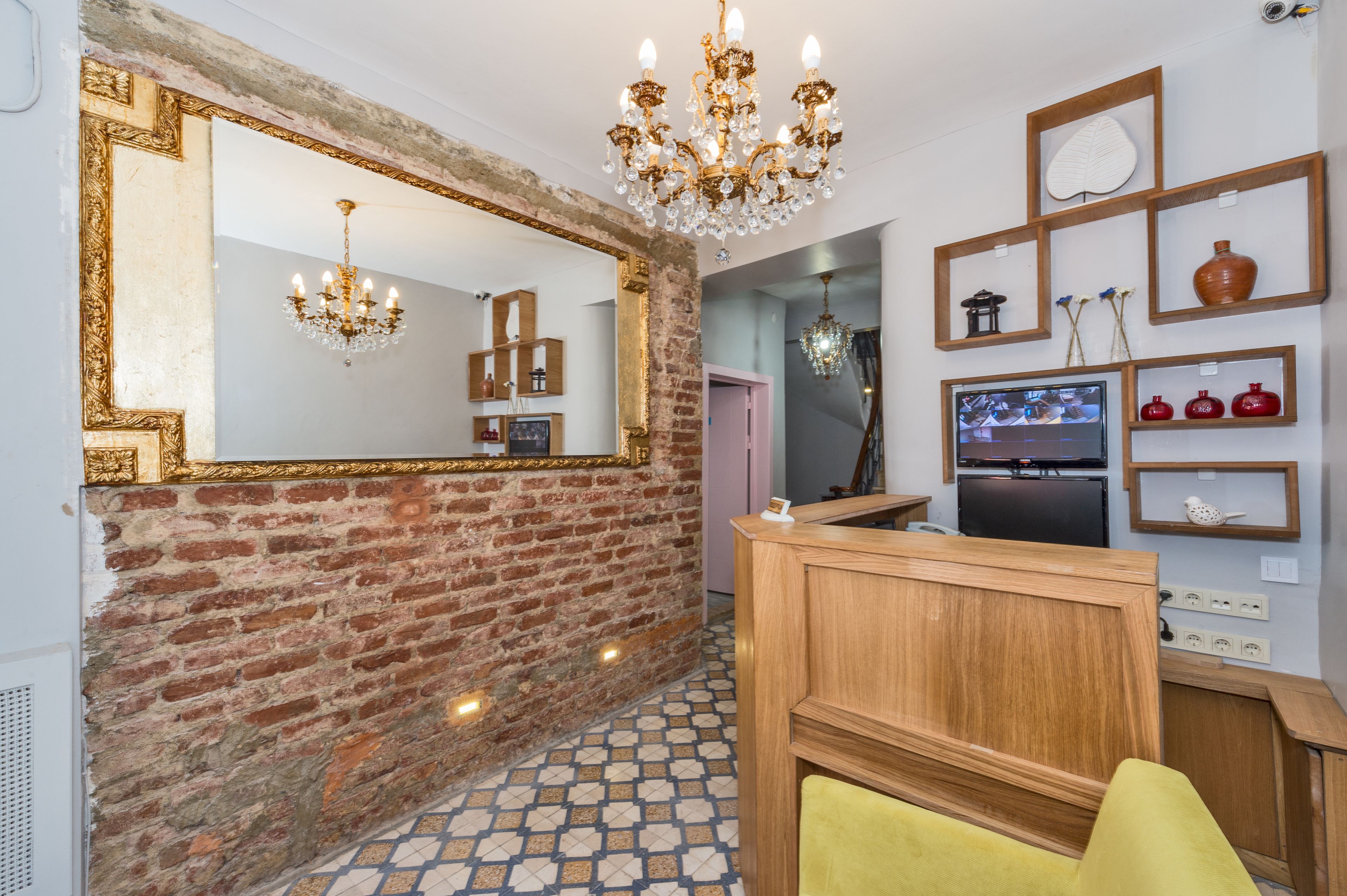 A room with a brick wall, a large mirror, a chandelier, wooden furniture, and a television.