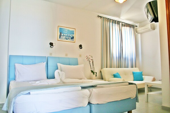 Una habitación de hotel con cama, sofá, una mesita y aire acondicionado.