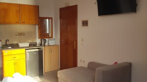 A compact living space with a kitchenette, a sofa, a TV, and a striped rug. - Domna Studios (Rhodes)