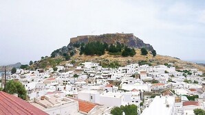 A coastal town with white buildings, a prominent hill with a fort, and a view of the sea. - Domna Studios (Rhodes)