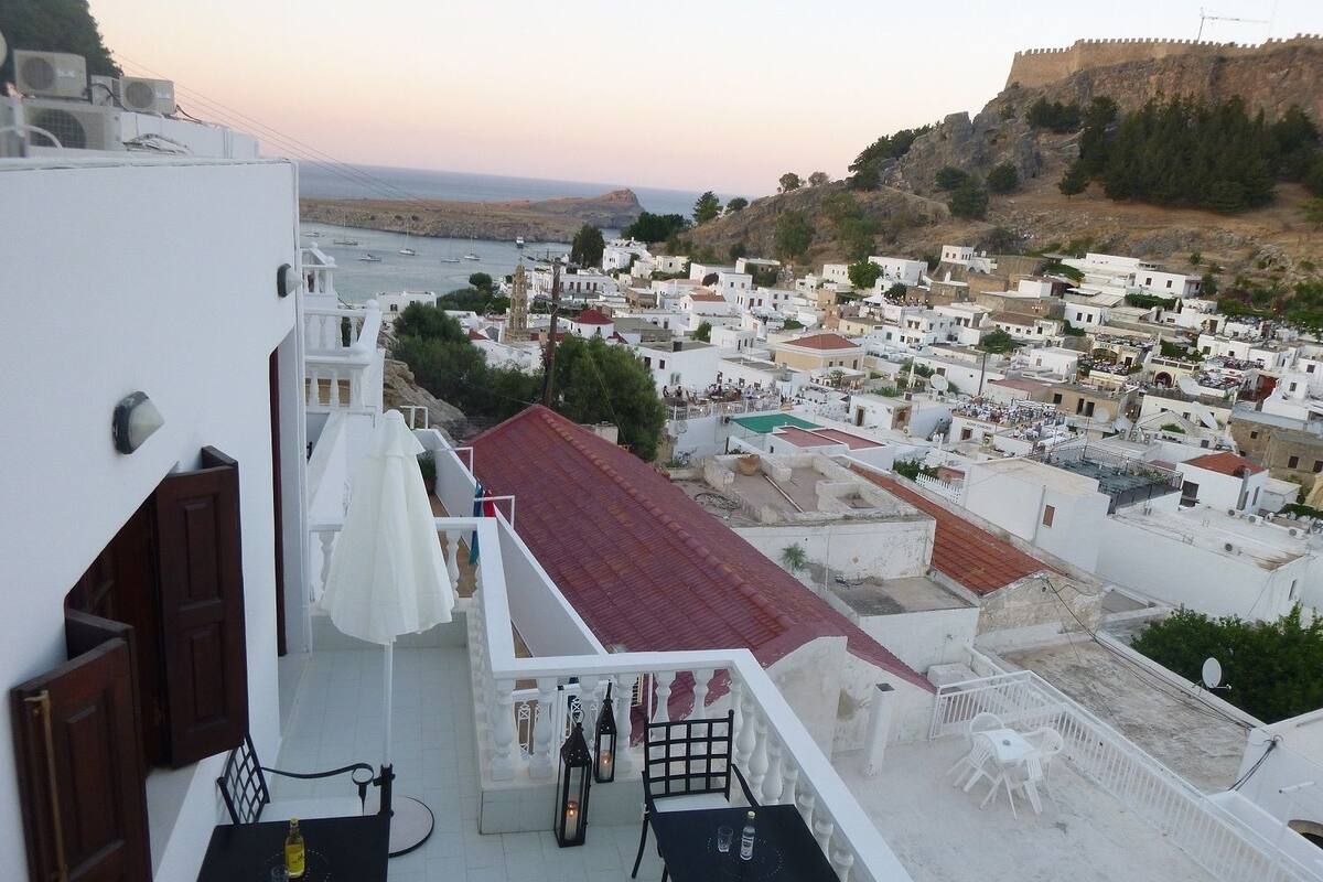 Una terraza en la azotea con mesa y sillas, con vistas a un pueblo costero de edificios blancos y una fortaleza en la colina.