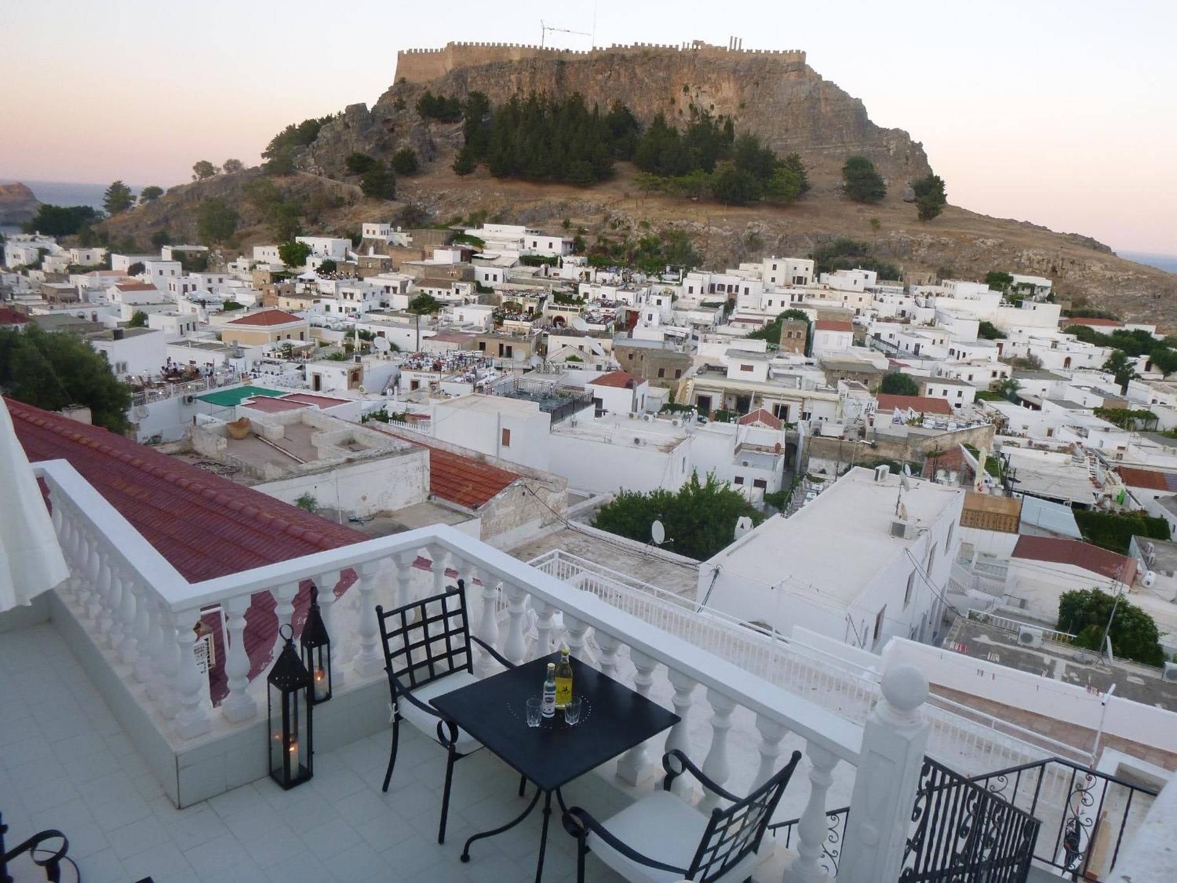 Terraza con mesa y sillas con vista a un pueblo de edificios blancos y una fortaleza en la colina.