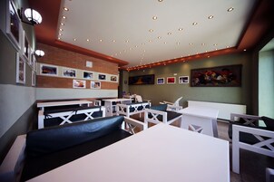 Un restaurante con mesas blancas y bancos acolchados de color negro, una pared de acento de ladrillo y un cuadro grande en la pared del fondo.