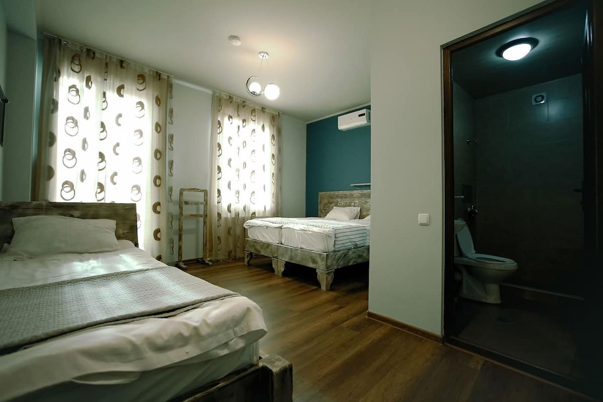A bedroom with two beds, a bathroom with a toilet, and a ceiling light fixture.