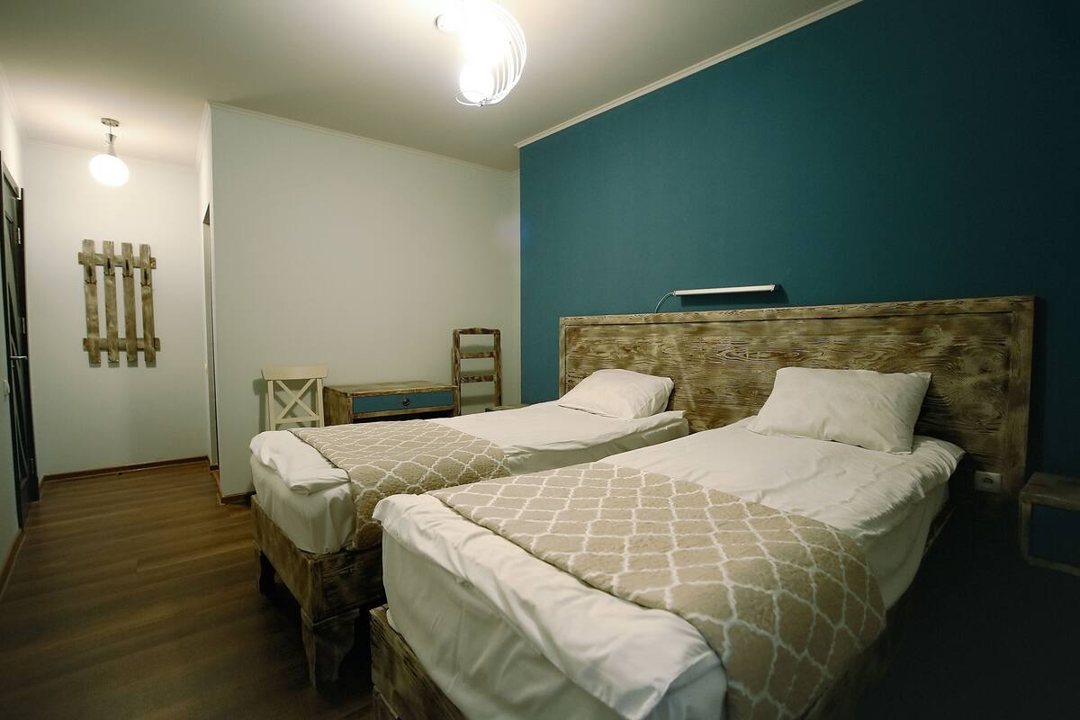 A room with two beds, a wooden headboard, a small table, and a wall-mounted light fixture.