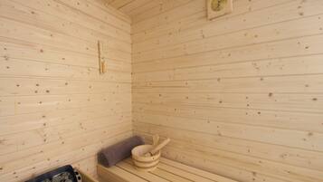 Una sauna de madera con un banco, un cubo de madera y una cuchara para servir, además de un termómetro en la pared.