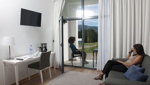 A modern hotel room with a desk, chair, and a sofa. There's a large window with a view of greenery and a mountain. - Hotel Parque Serra da Lousã (Miranda do Corvo)