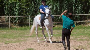 A person riding a white horse in an outdoor area with a dirt ground and a wooden fence.