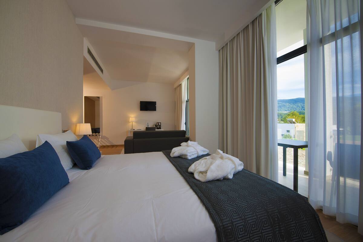 A hotel room with a large bed, a desk, a TV, and a balcony with a view.