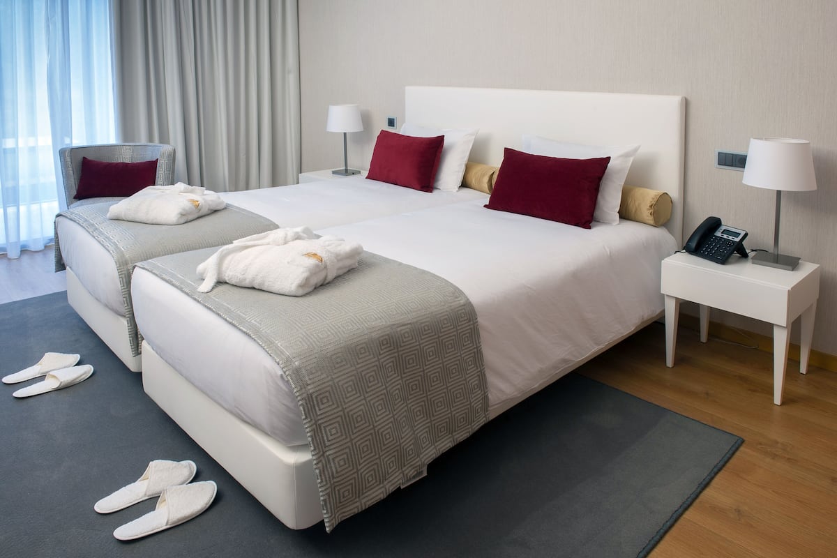A hotel room with two beds, a bedside table with a phone, and slippers on the floor.