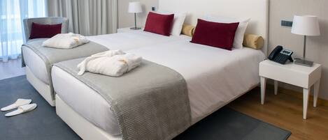 A hotel room with two beds, a bedside table with a phone, and slippers on the floor.