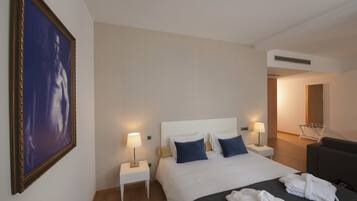 A hotel room with a large bed, two bedside tables with lamps, a dark-colored sofa, and a framed picture on the wall.