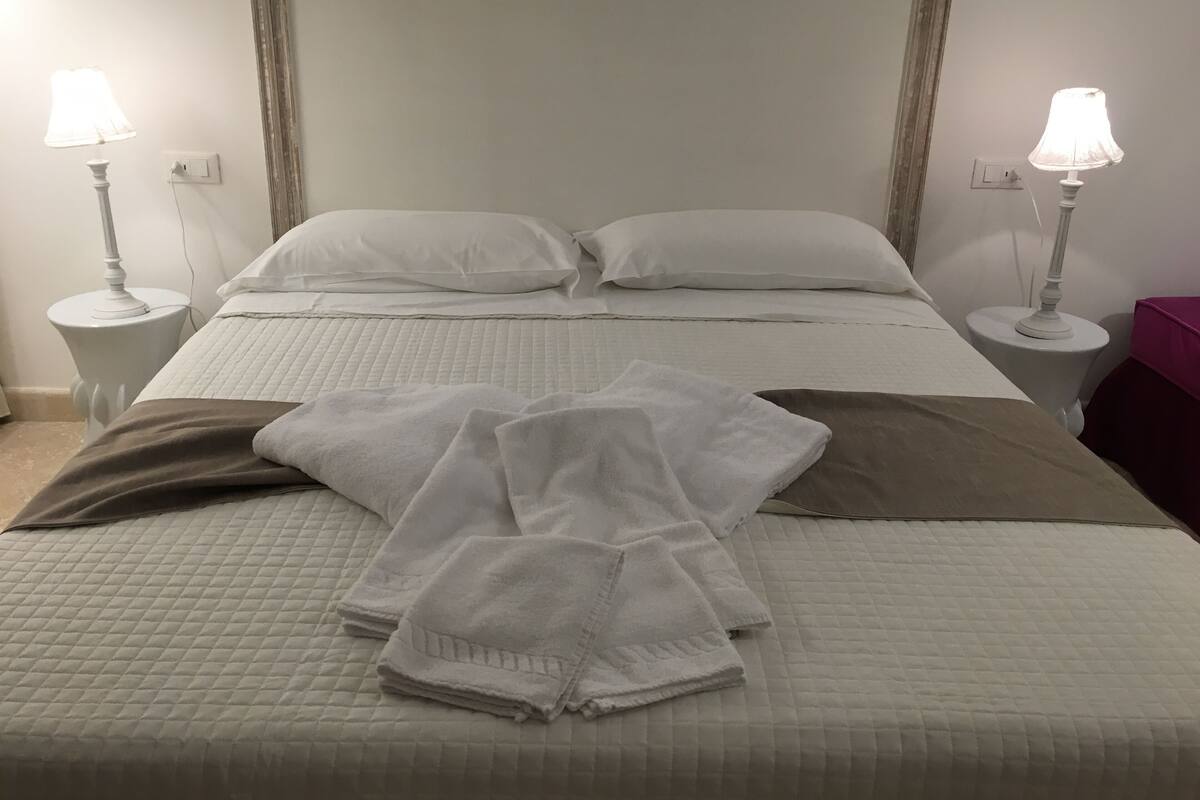 A neatly made bed with white linens and a brown blanket, flanked by two bedside lamps on white nightstands.