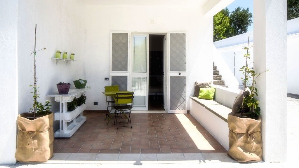 A small patio area with a table and chairs, potted plants, and a door leading to an interior space.