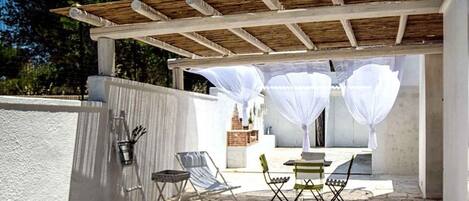 Un patio exterior con una pérgola, paredes blancas y una mesa con sillas.
