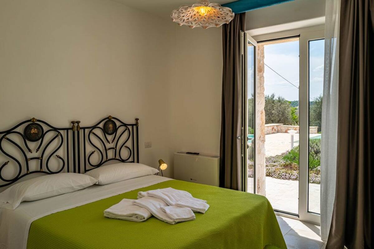 A bedroom with a green bedspread, a metal headboard, white pillows, and a nightstand with a lamp.