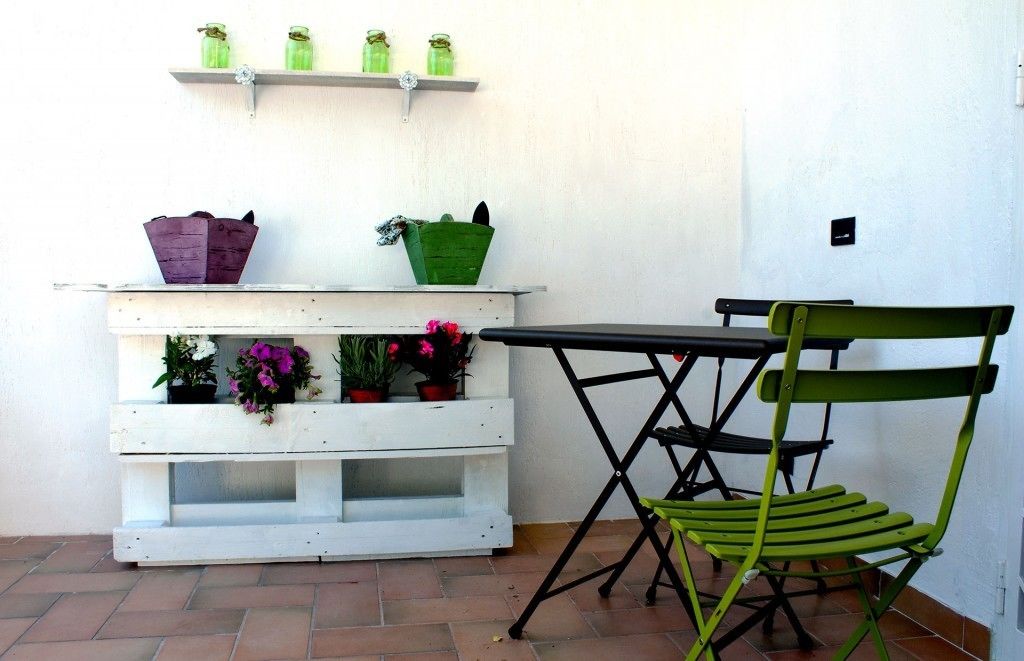 A white wooden bench with potted plants and a green folding chair.