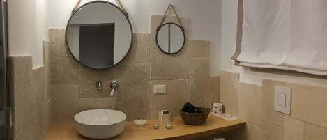 A bathroom with a round sink, two mirrors, a wooden countertop, a towel rack, and a towel hanging on the wall.