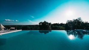 Una piscina azul cristalina con una estructura de techo de paja a la izquierda y un paisaje verde exuberante al fondo.
