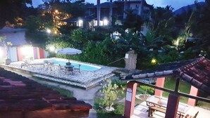 A pool area with lounge chairs and a table, surrounded by greenery and a stone pathway. - Delta Mar Maresias (São Sebastião)