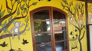 A room with a yellow wall featuring a mural of a monkey on a tree branch, a bird in a cage, and an owl in a tree. - Delta Mar Maresias (São Sebastião)