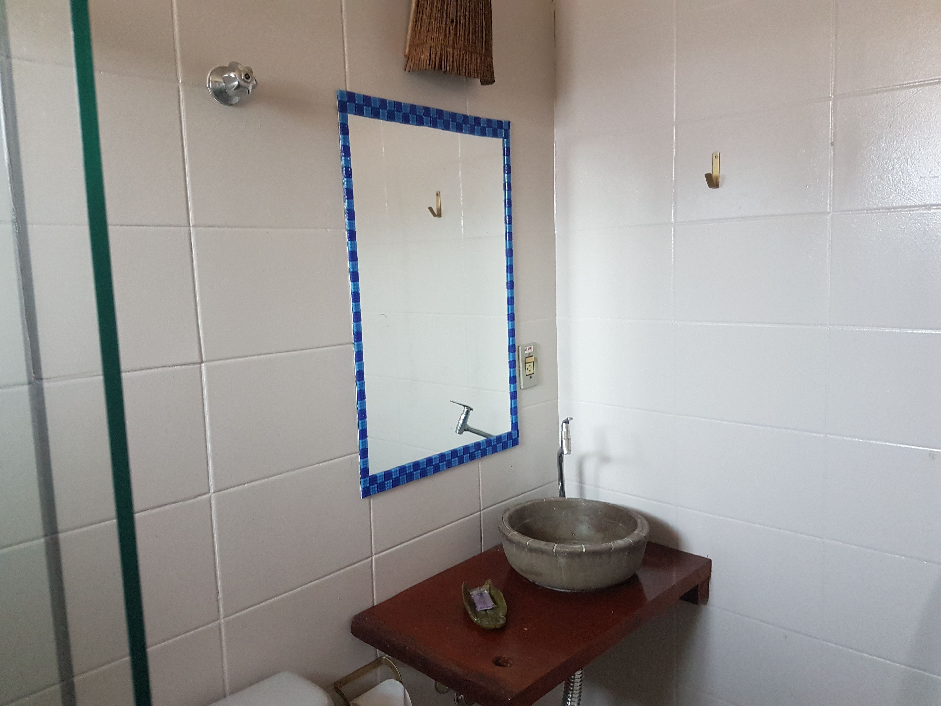 Un baño con paredes de azulejos blancos, un espejo con marco azul a cuadros, un lavabo redondo sobre una encimera de madera y una ducha con puerta de cristal.