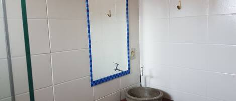Un baño con paredes de azulejos blancos, un espejo con marco azul a cuadros, un lavabo redondo sobre una encimera de madera y una ducha con puerta de cristal.